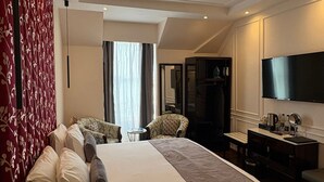 A hotel room with a large bed, a desk with a flat-screen TV, a chair, and a small table.