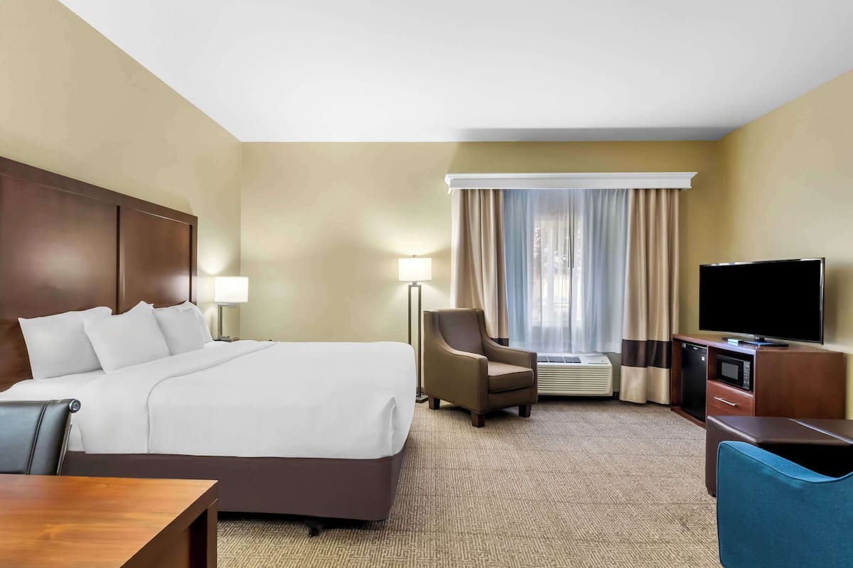 Une chambre d’hôtel avec un grand lit, un bureau, une chaise, une télévision et une fenêtre avec des rideaux.