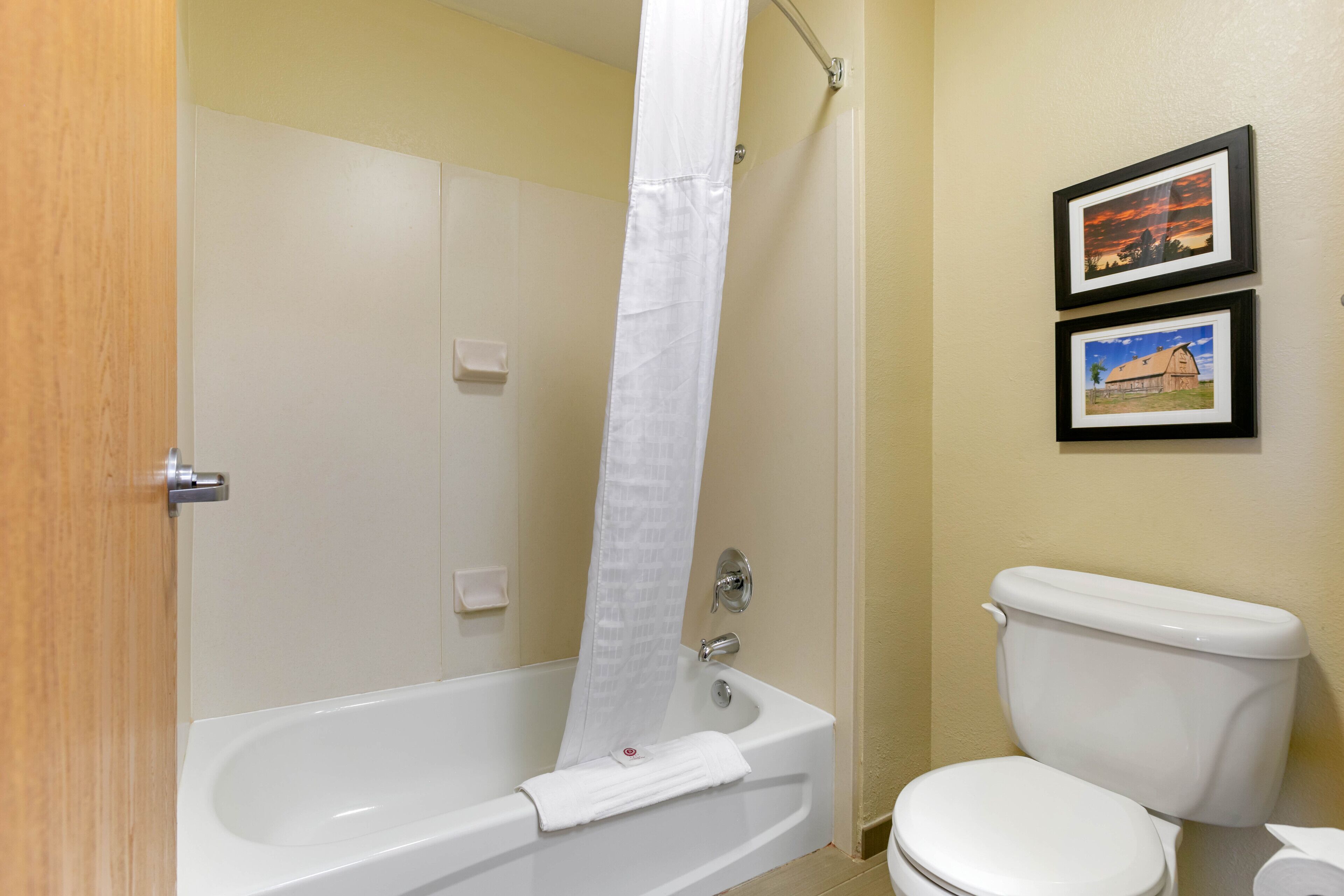 A bathroom with a bathtub, toilet, and two framed pictures on the wall.