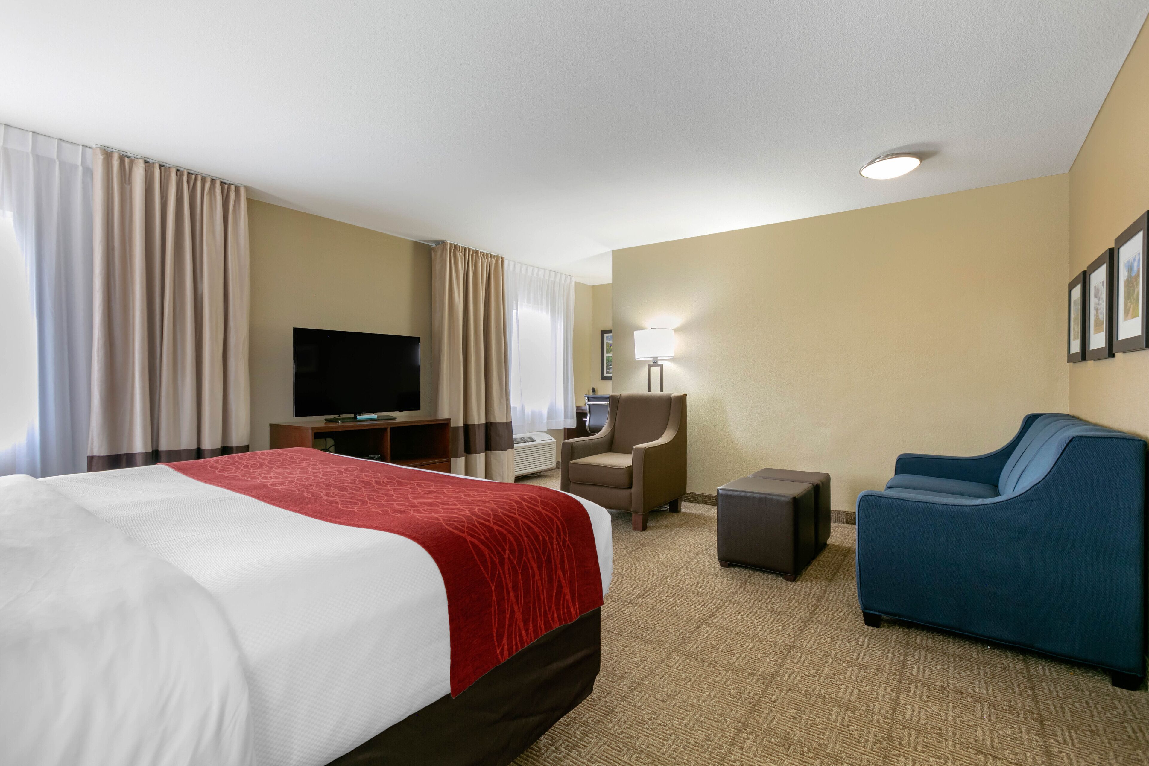 Una habitación de hotel con una cama grande, un escritorio con televisión de pantalla plana, una silla, un sofá y una lámpara.