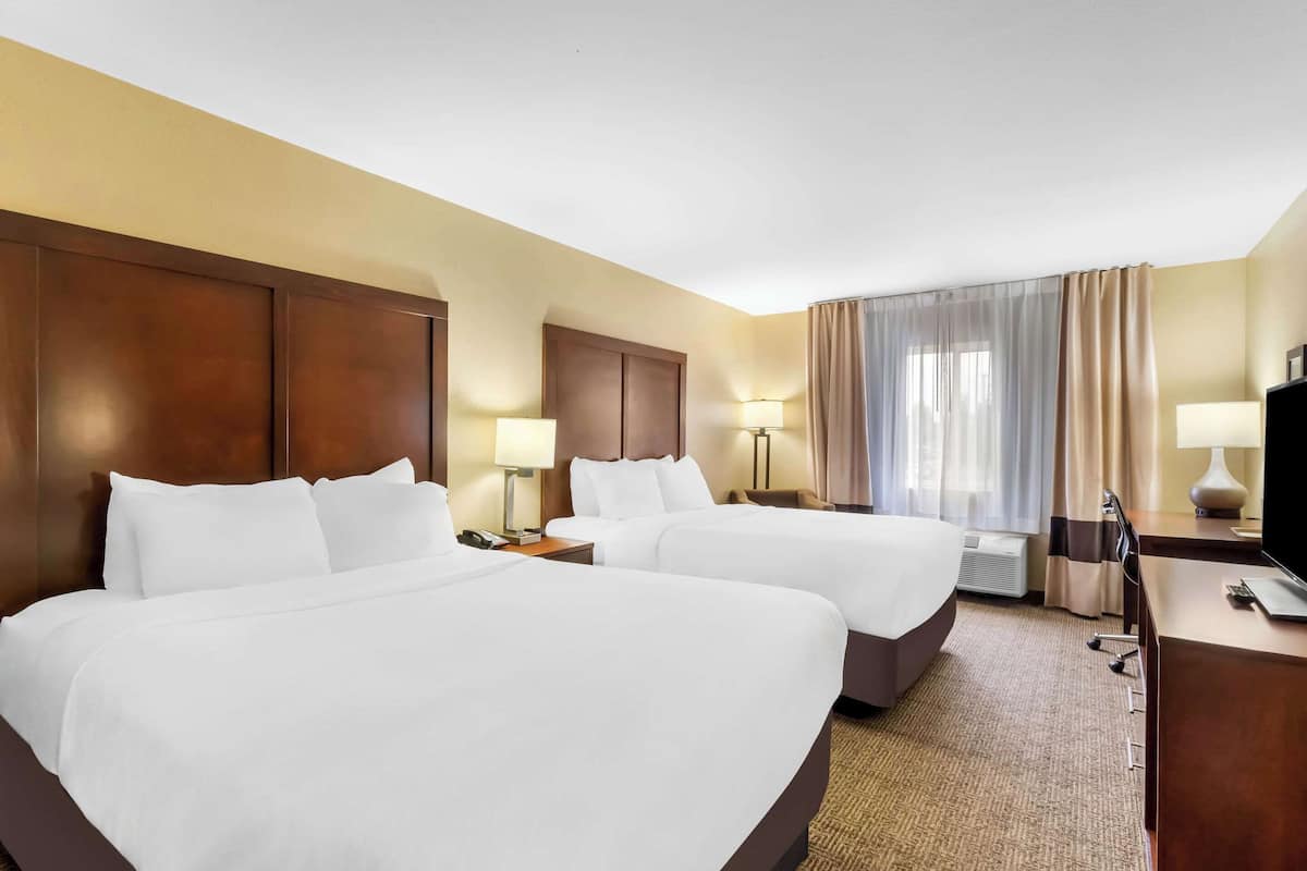 Une chambre d’hôtel avec deux lits, un bureau, une télévision et une fenêtre avec des rideaux.