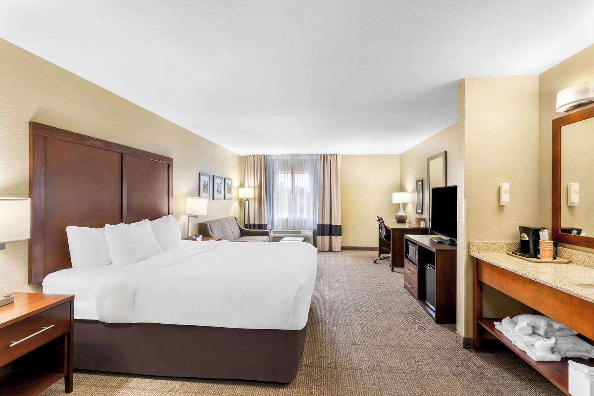 Une chambre d’hôtel comprenant un grand lit, un bureau, une chaise, une télévision, une lampe de bureau, un miroir et un meuble-lavabo dans la salle de bain.