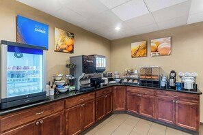 A kitchen area with a refrigerator, coffee machine, and various food items on the counter.