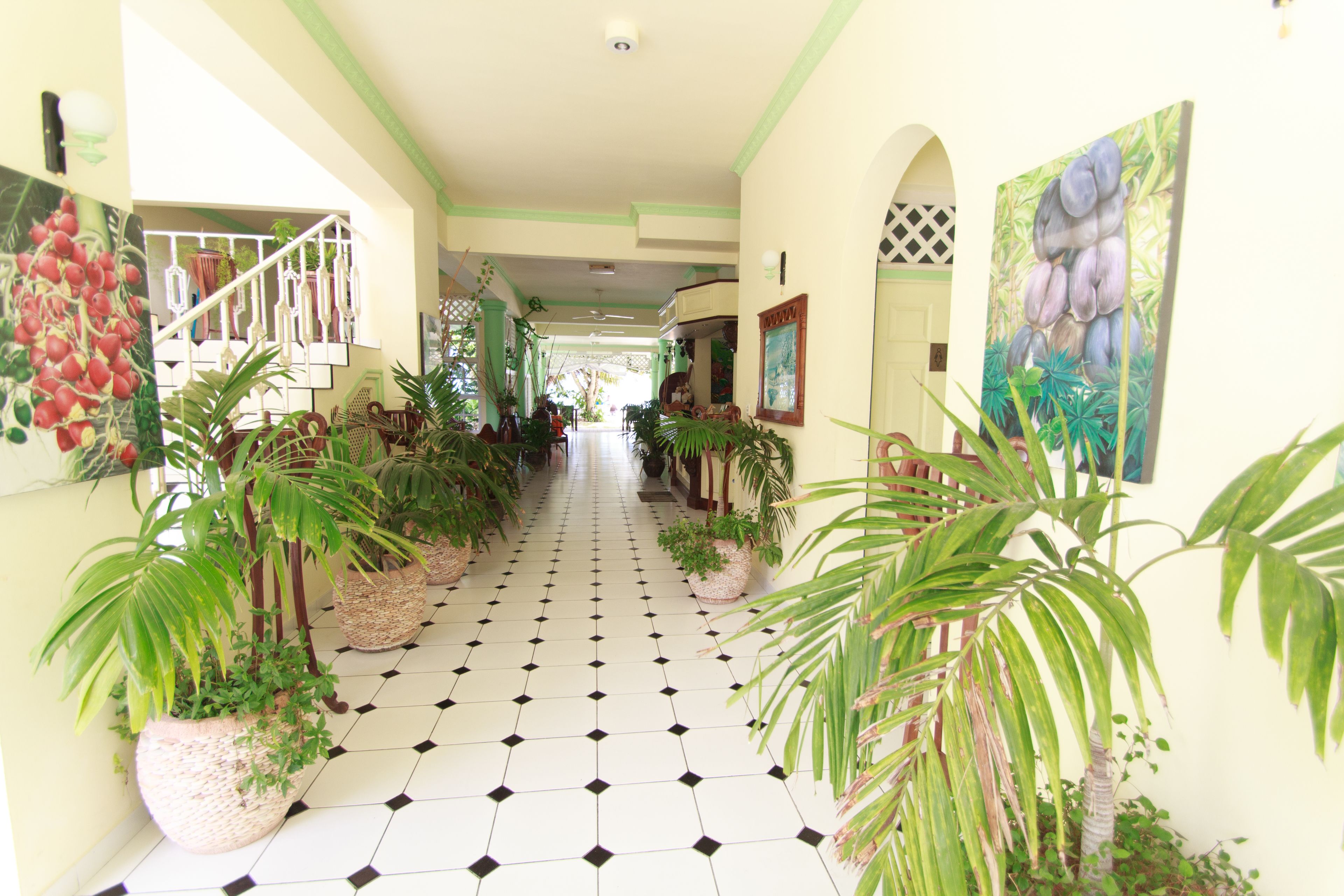 A hallway with a tiled floor, potted plants, and artwork on the walls.
