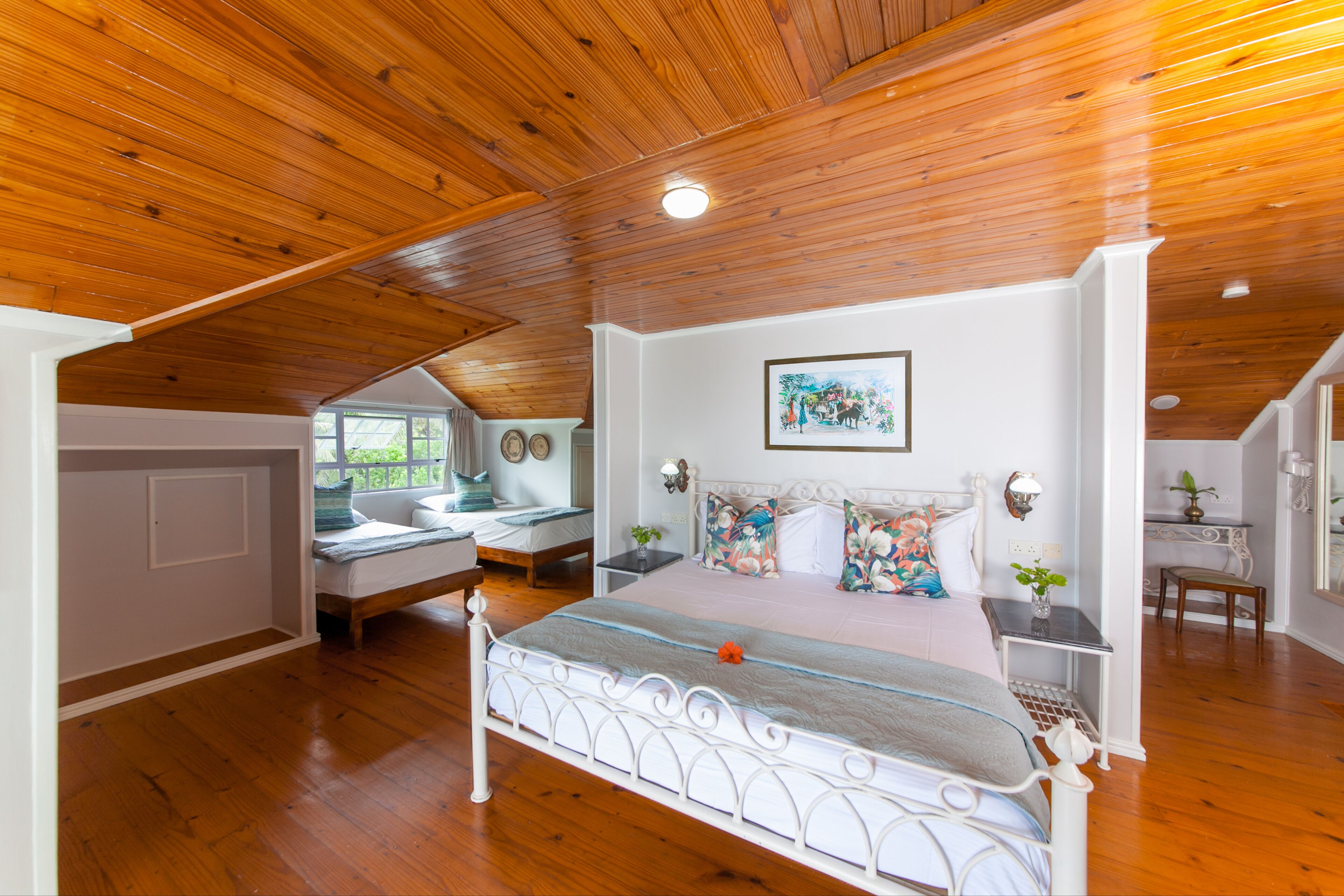 Un dormitorio con techo de madera, una cama grande con estructura blanca, una mesita de noche con lámpara y una ventana con cortinas.