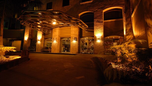 A hotel entrance with a covered walkway, palm trees, and a well-lit facade. - Hotel Celta (Zapopan)