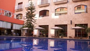 A hotel pool area with a tiled floor, outdoor seating, and a building with balconies. - Hotel Celta (Zapopan)