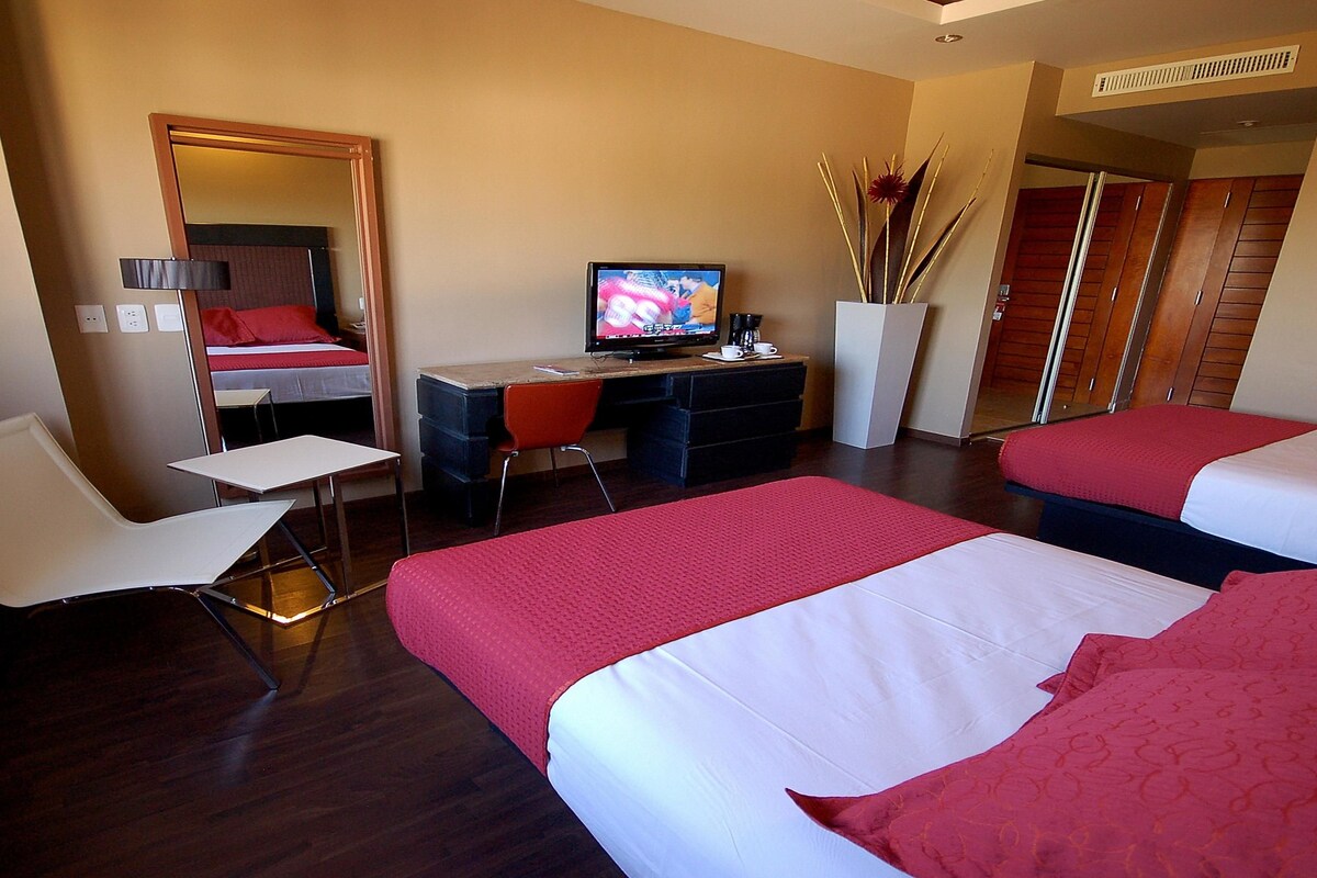 A hotel room with two beds, a desk with a computer, a chair, and a mirror.