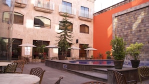 An outdoor patio area with tables and chairs, a small pool, and potted plants. - Hotel Celta (Zapopan)