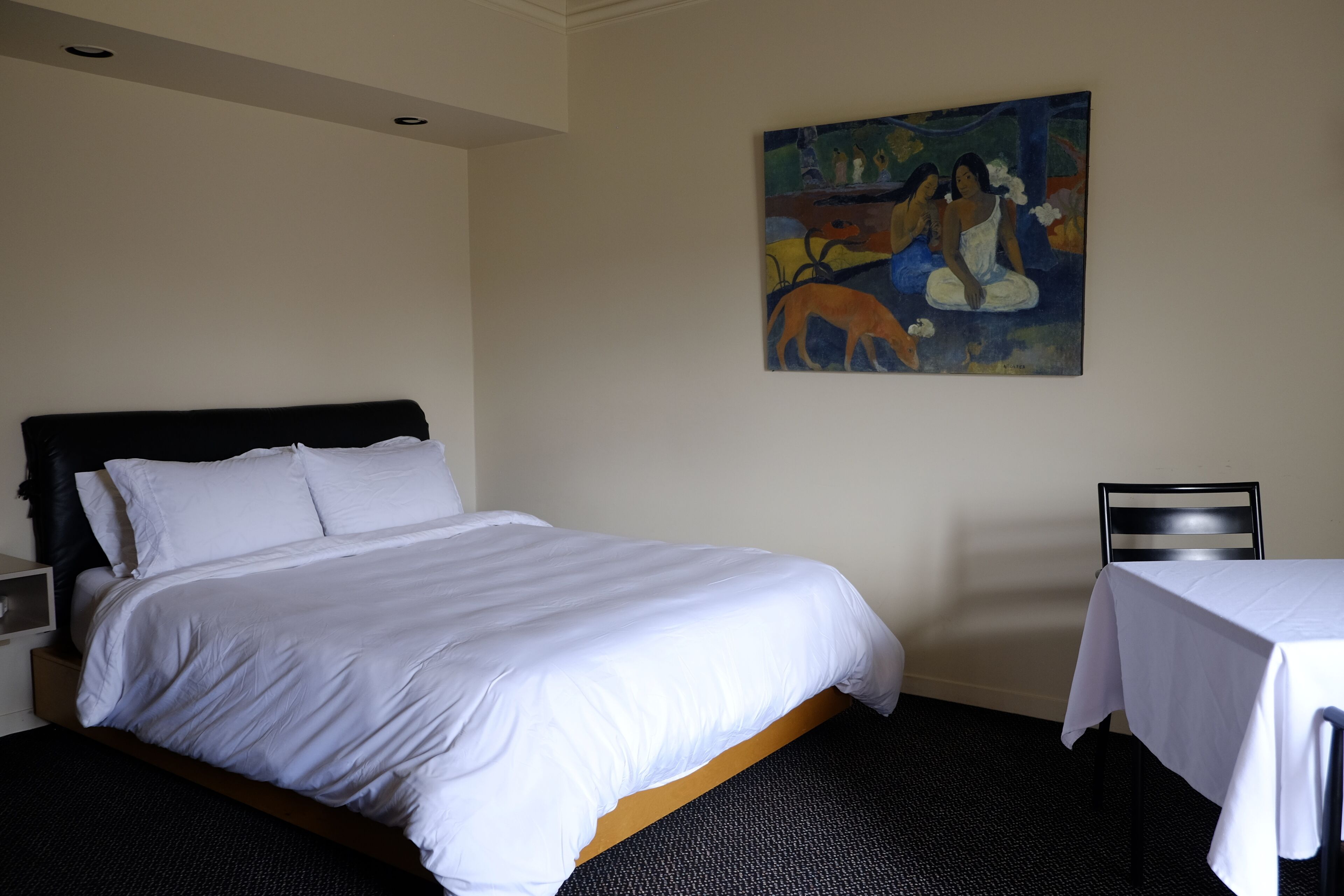 Une chambre d’hôtel avec un lit, un tableau au mur, une petite table et une chaise.