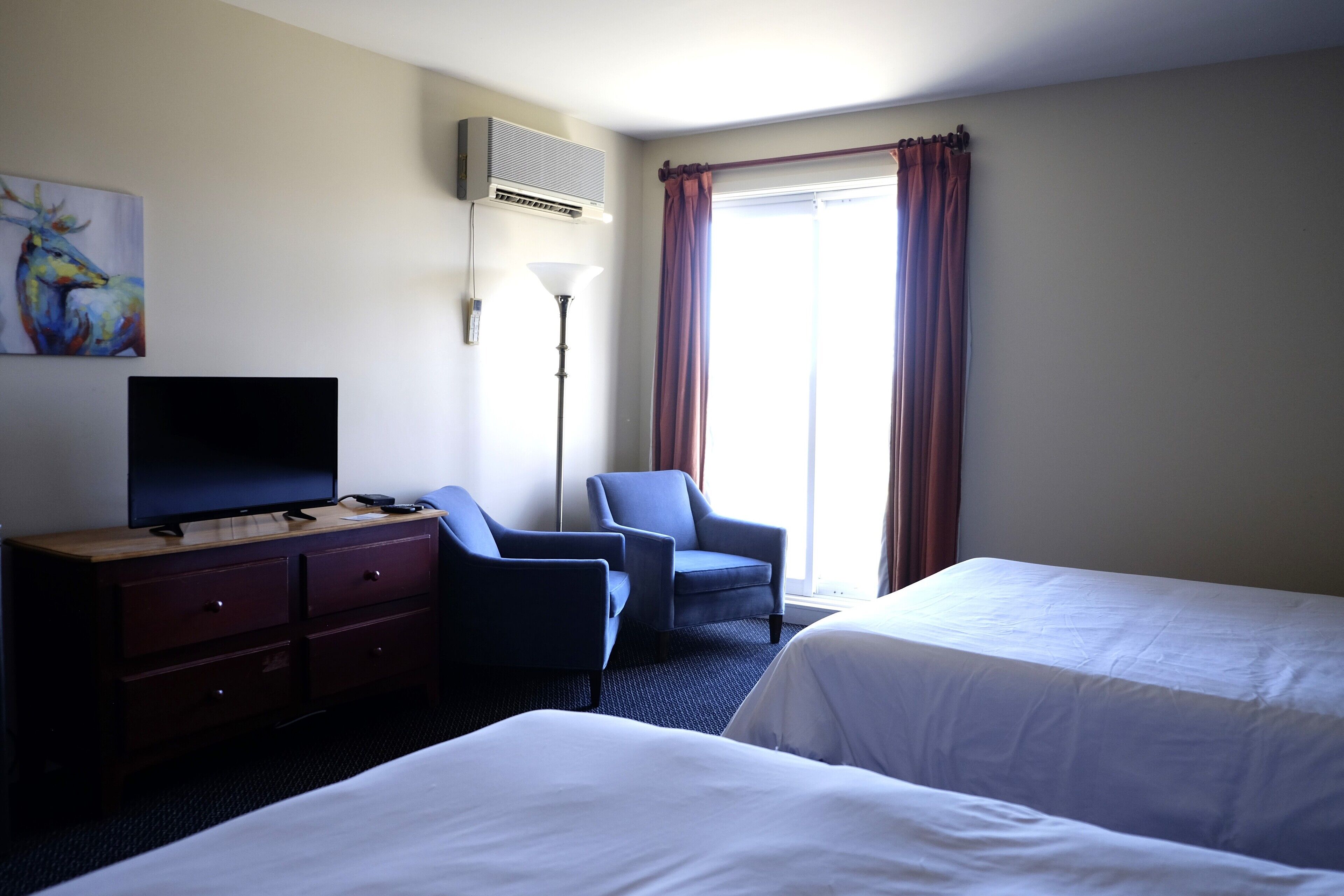Een hotelkamer met twee bedden, een televisie, een bureau met lades, een lamp en een schilderij aan de muur.