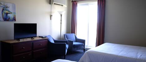 A hotel room with two beds, a TV, a desk with drawers, a lamp, and a painting on the wall.