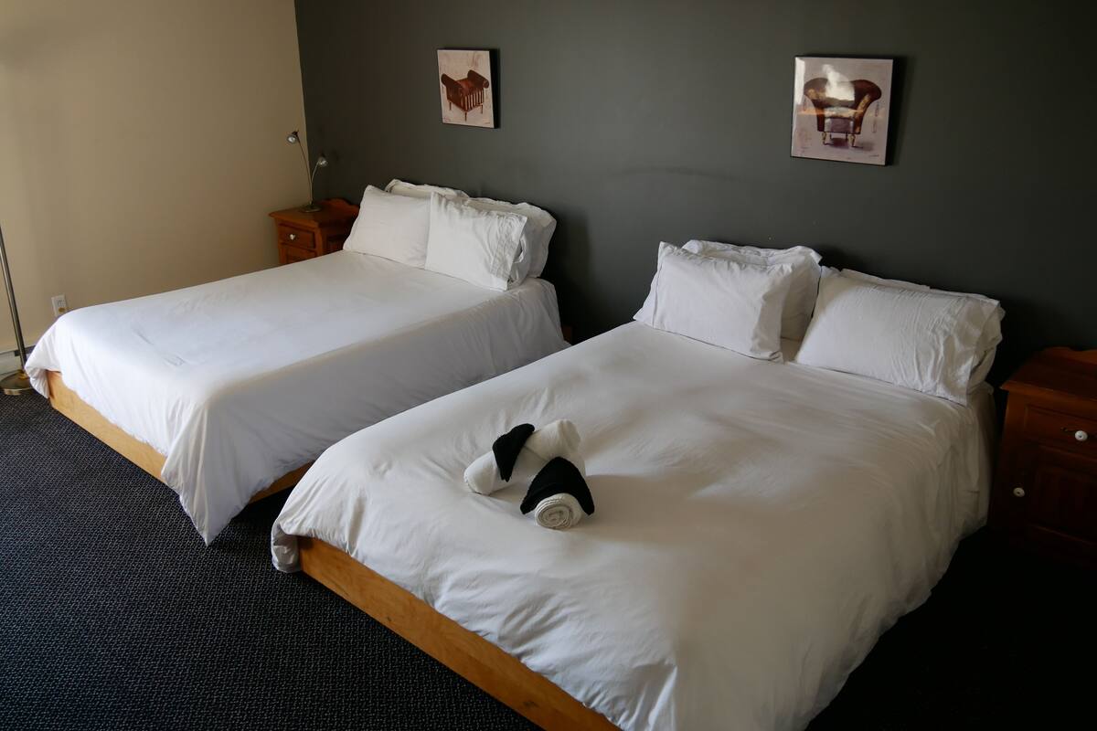 Habitación de hotel con dos camas individuales, una pared oscura y dos cuadros enmarcados.