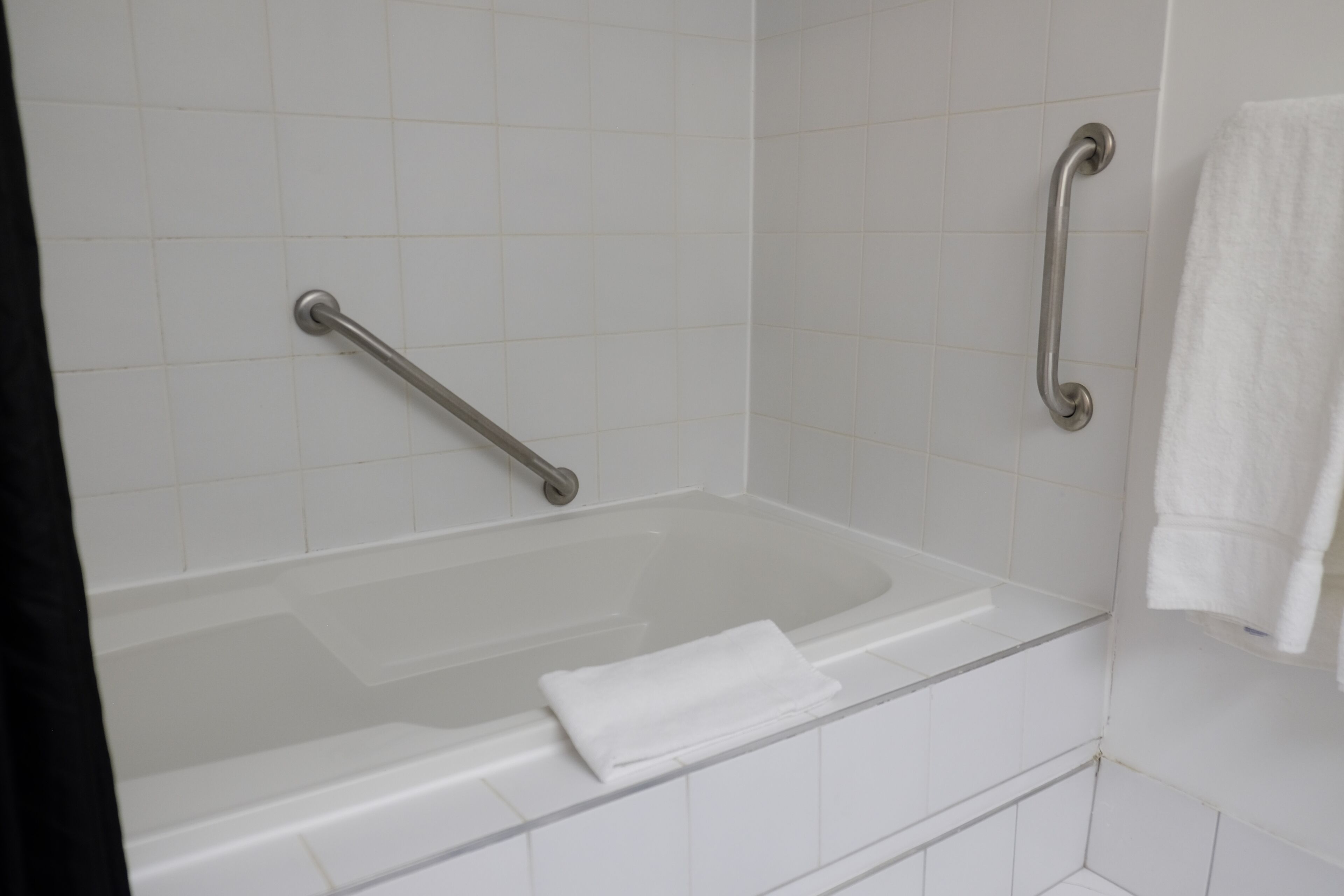 Una bañera blanca con una barra de apoyo a la izquierda y una toalla a la derecha.