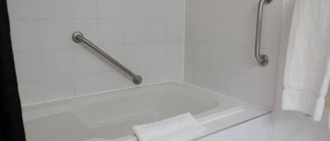 A white bathtub with a grab bar on the left and a towel on the right.