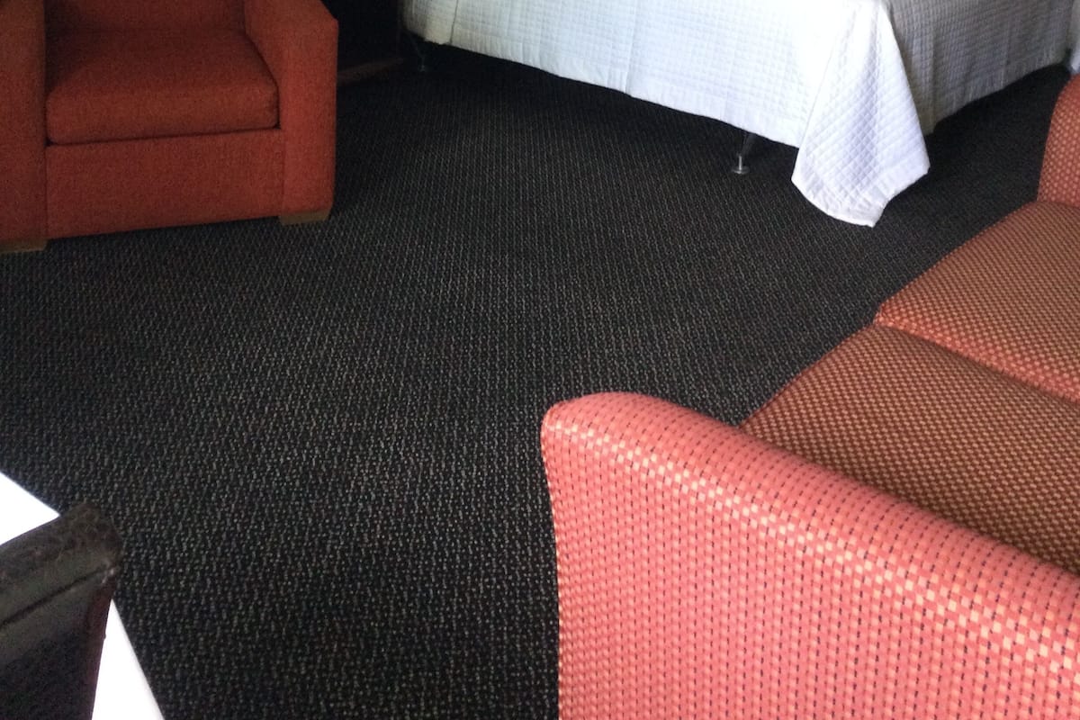 Una habitación de hotel con una cama, un sillón rojo, una mesita de noche y un armario.
