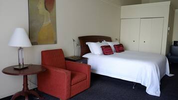 A hotel room with a bed, a red armchair, a lamp, a painting on the wall, and a wardrobe.
