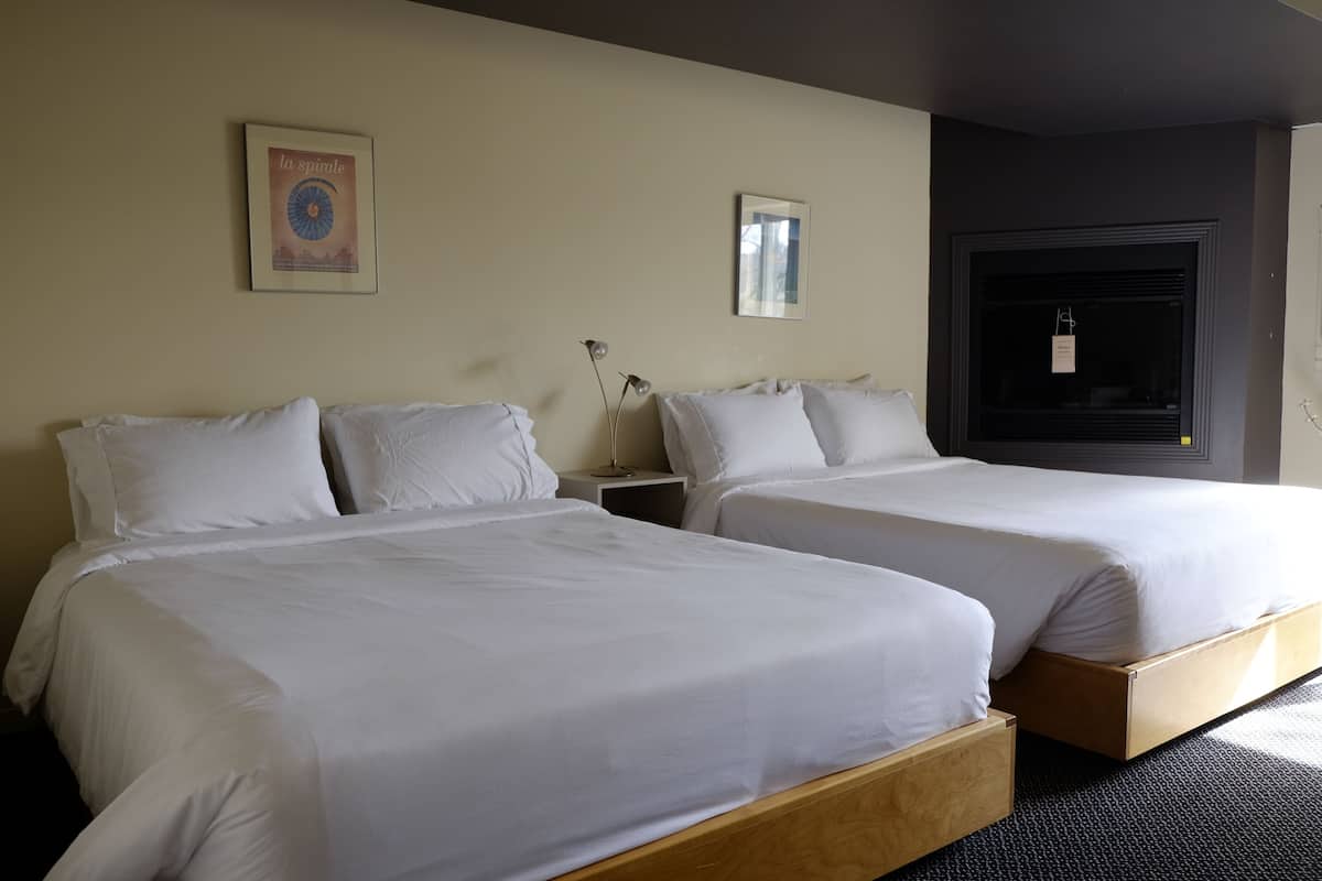Habitación de hotel con dos camas individuales, una mesita de noche, una lámpara, un cuadro en la pared y una ventana con vistas.