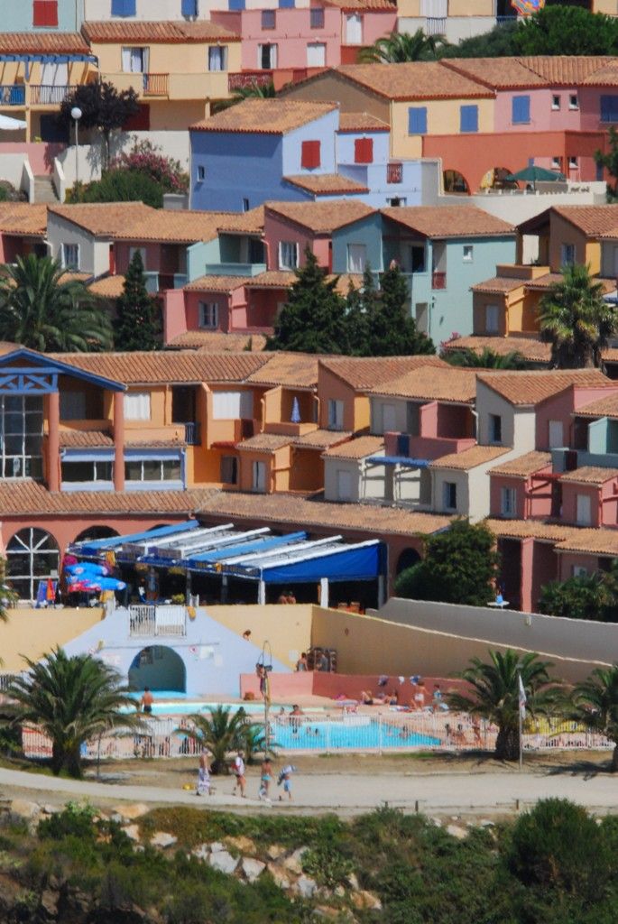 Un quartier résidentiel situé sur la côte, avec des bâtiments aux couleurs vives, une piscine et une plage.