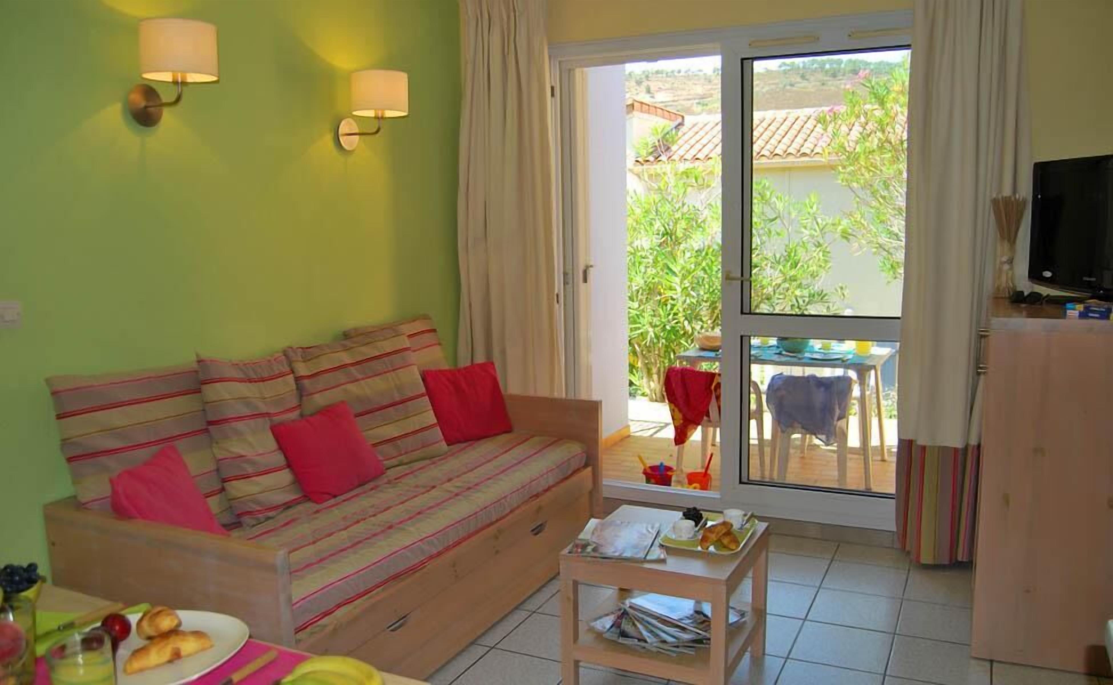 Un salón acogedor con un sofá, una mesa con alimentos para el desayuno y un ventanal corredizo que da a un espacio exterior.