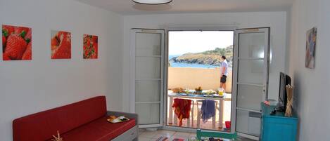 Una habitación con un sofá rojo, una mesa de comedor con desayuno y vistas a la playa.