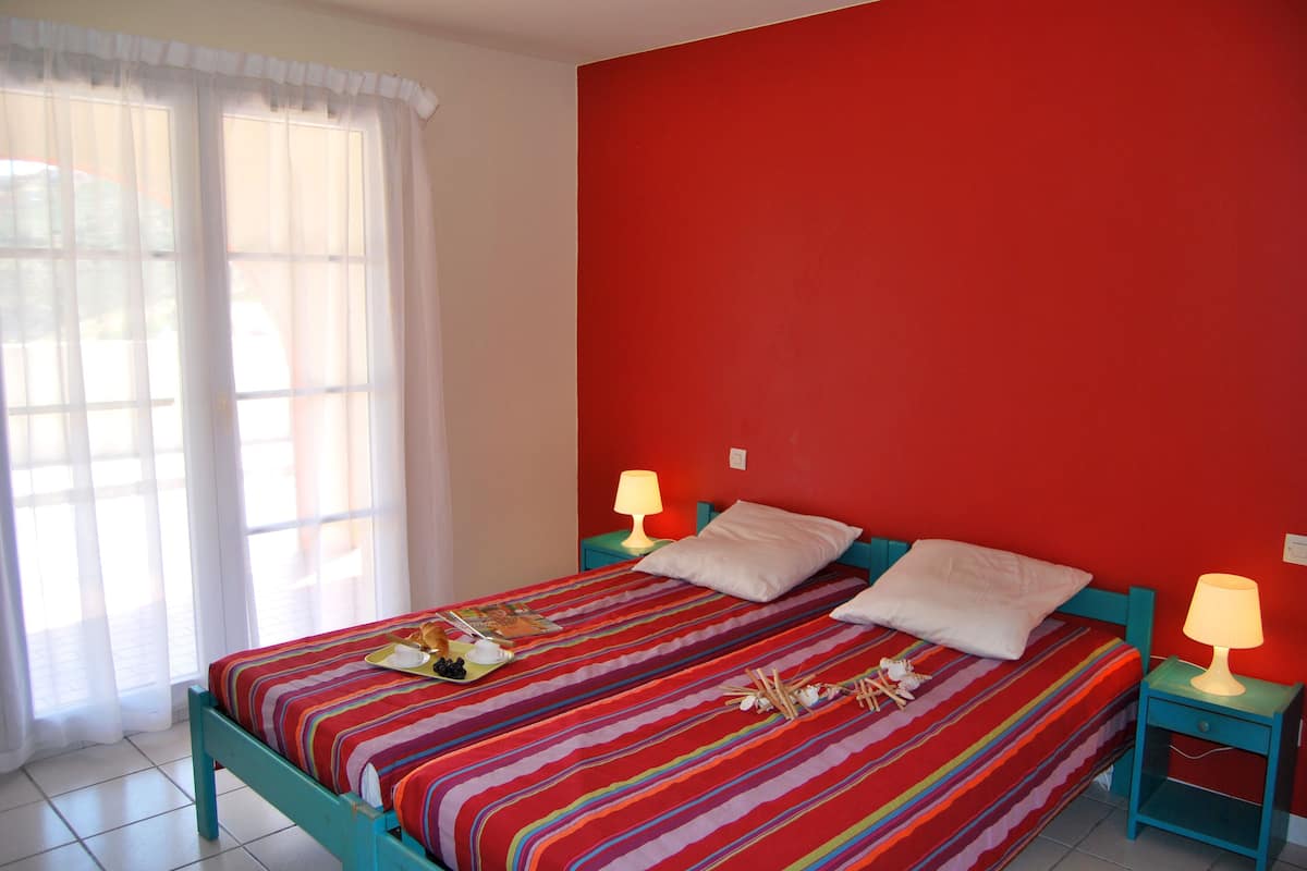 A bed with a colorful striped bedspread, two bedside lamps, and a window with sheer curtains.