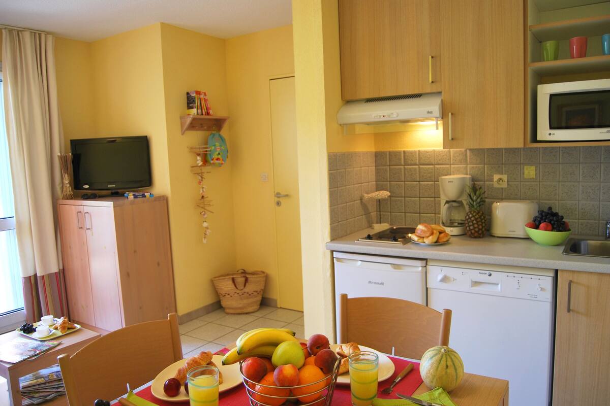 A compact kitchen with a dining area, equipped with a microwave, toaster, and a sink.