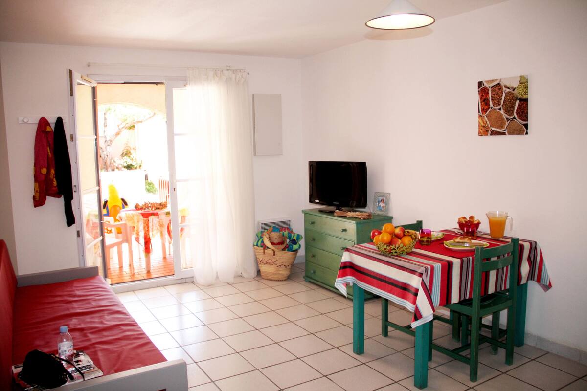 A room with a red sofa, a dining table with a red and white tablecloth, a green cabinet, and a television on top.