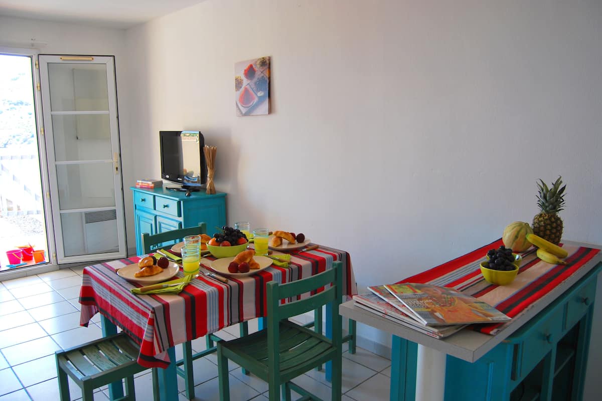 A dining area with a table set for breakfast, including plates of food and a fruit bowl.