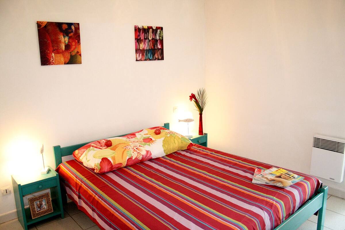 Une chambre à coucher comprenant un lit, deux tables de chevet, un radiateur fixé au mur et deux œuvres d’art murales.
