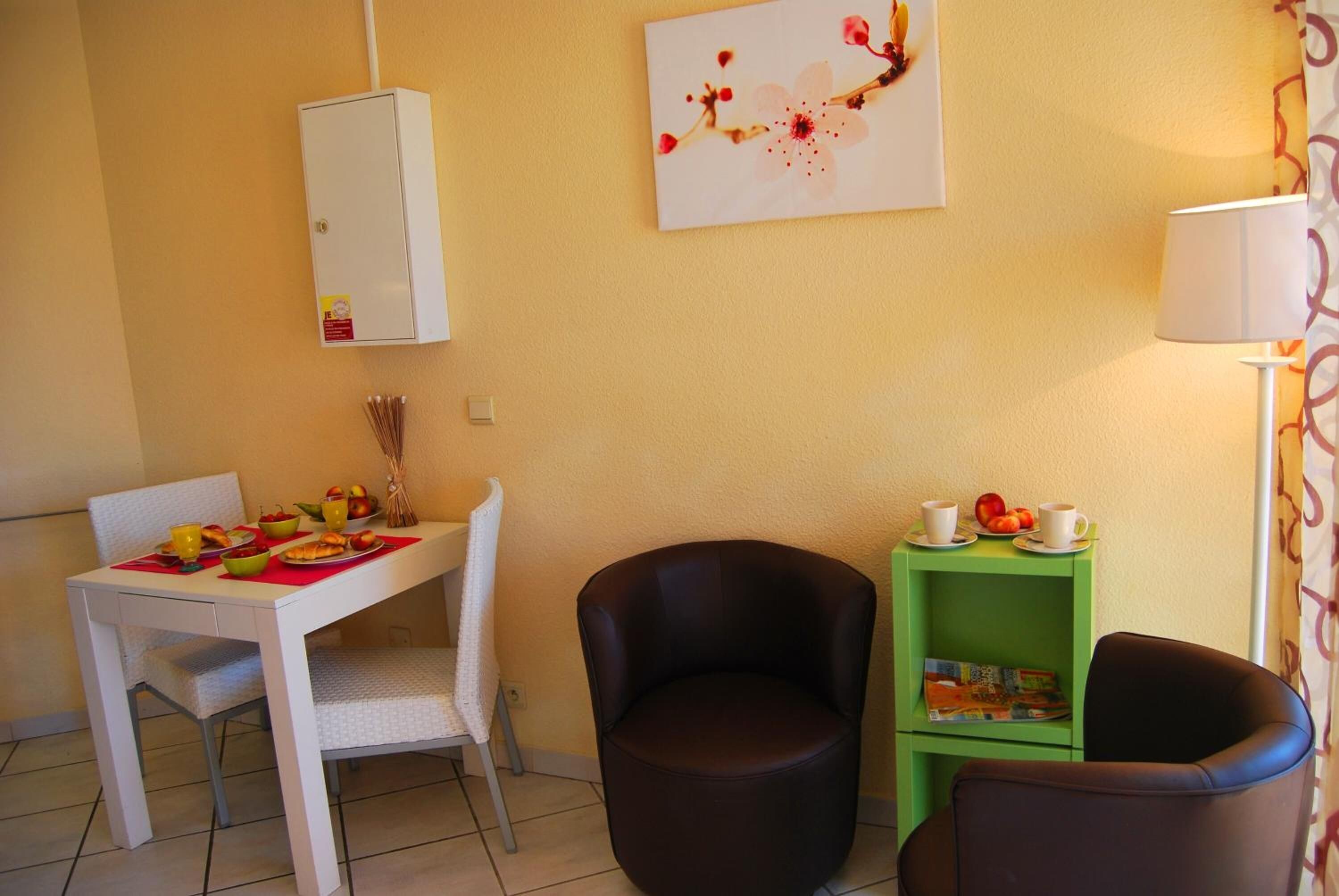 A dining area with a white table set for breakfast, a green side table with a magazine, and two brown chairs.