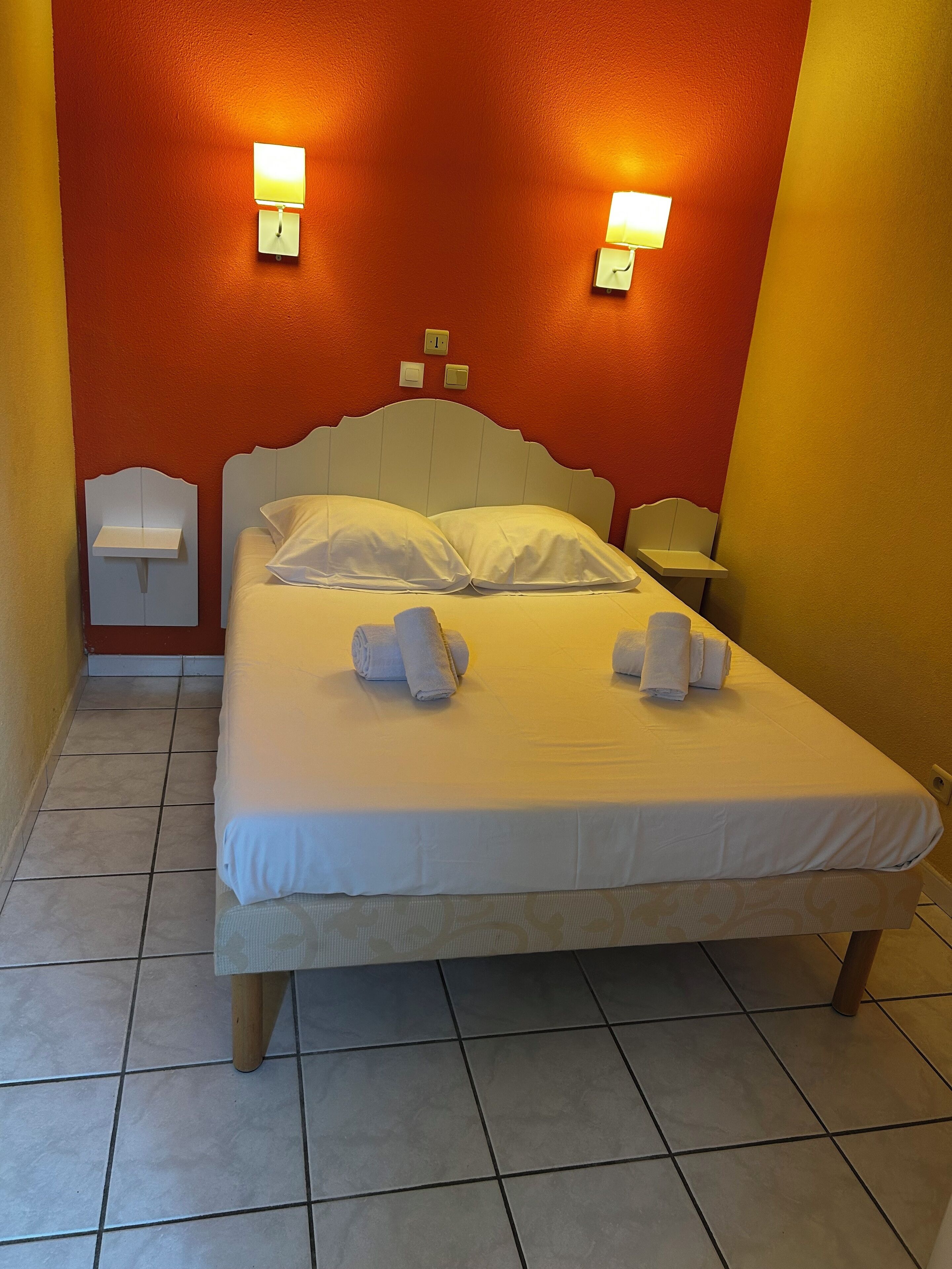 Una habitación de hotel con una cama, dos mesitas de noche y dos lámparas de pared.