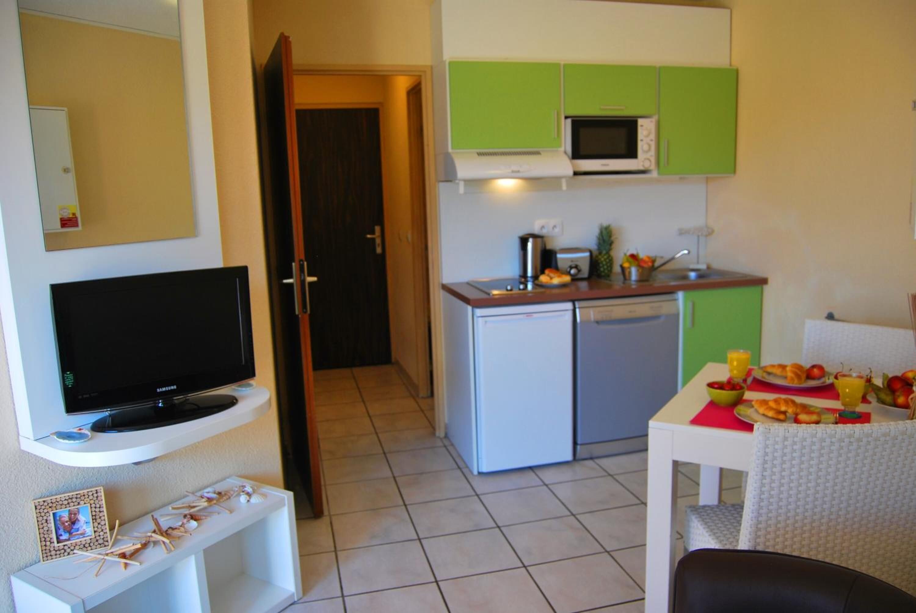 A compact living space with a TV on a stand, a small kitchenette with a microwave and a mini-fridge, and a dining area with a table and chairs.