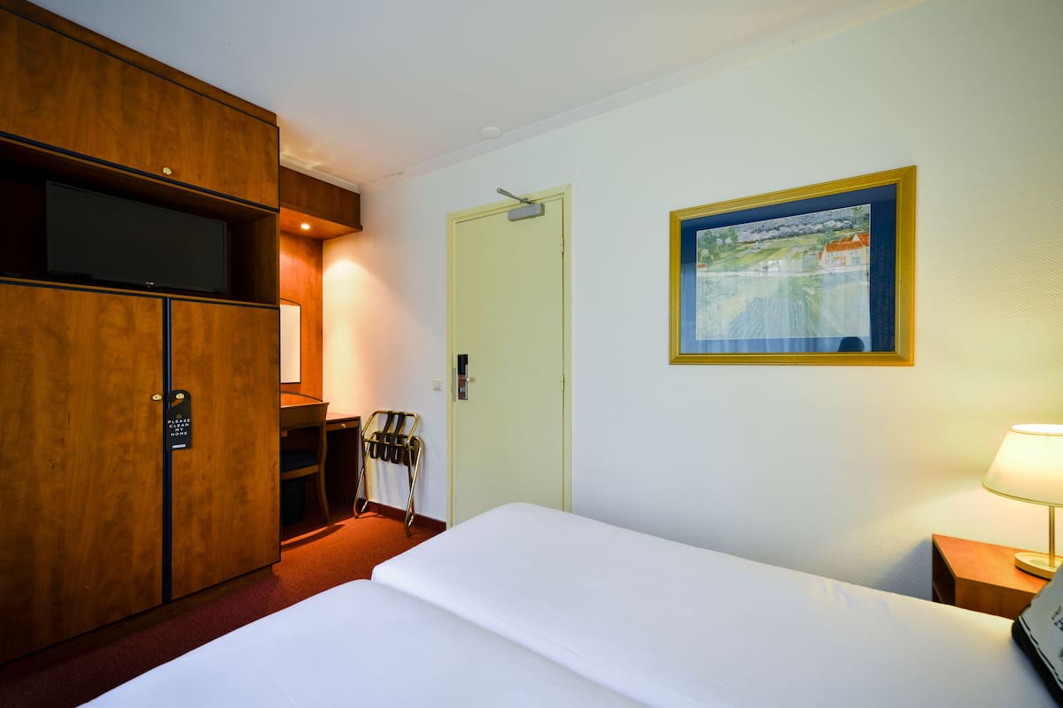 Ein Hotelzimmer mit einem Bett, einem Schreibtisch mit Fernseher, einer Tür und einem gerahmten Bild an der Wand.