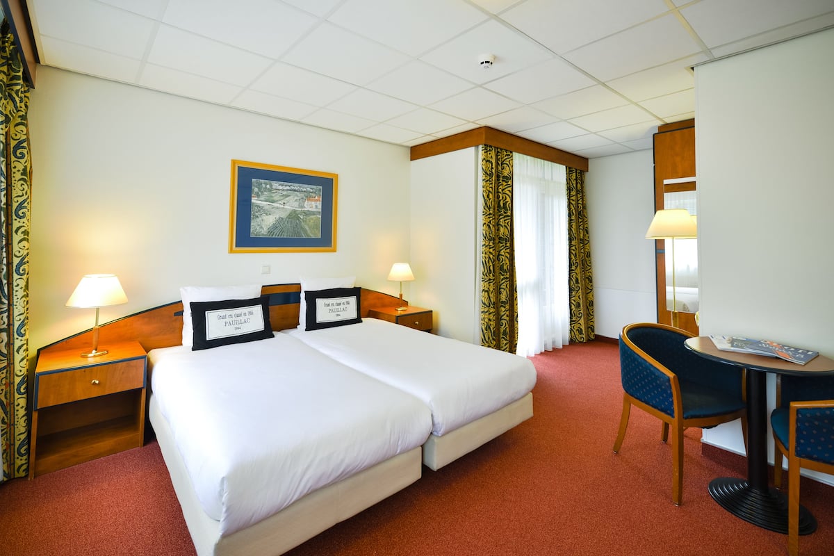 Ein Hotelzimmer mit zwei Betten, einem Schreibtisch mit Stuhl, einer Lampe und einem gerahmten Bild an der Wand.