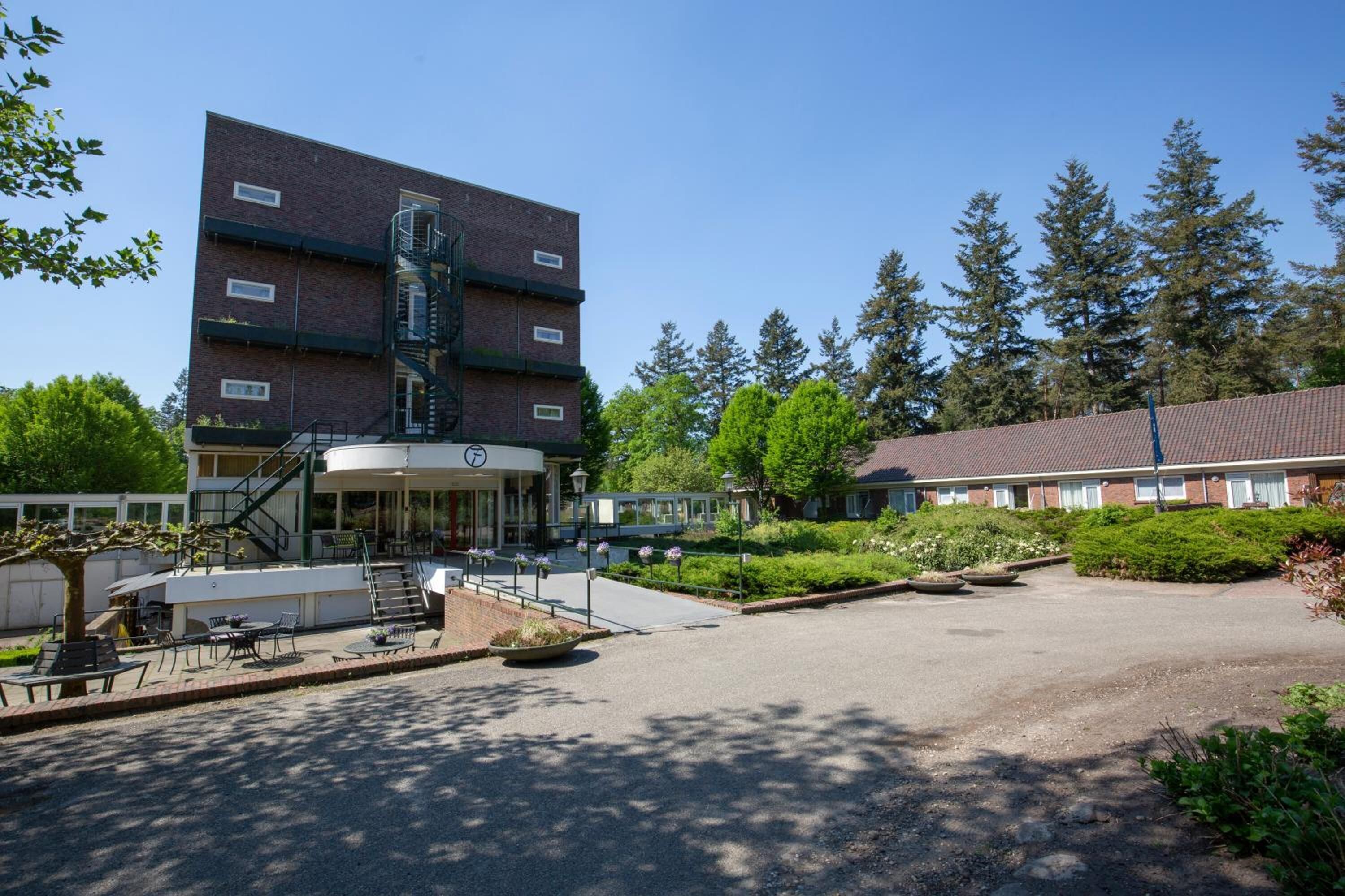 A building with a brick facade, a covered entrance, and a landscaped courtyard with outdoor seating.