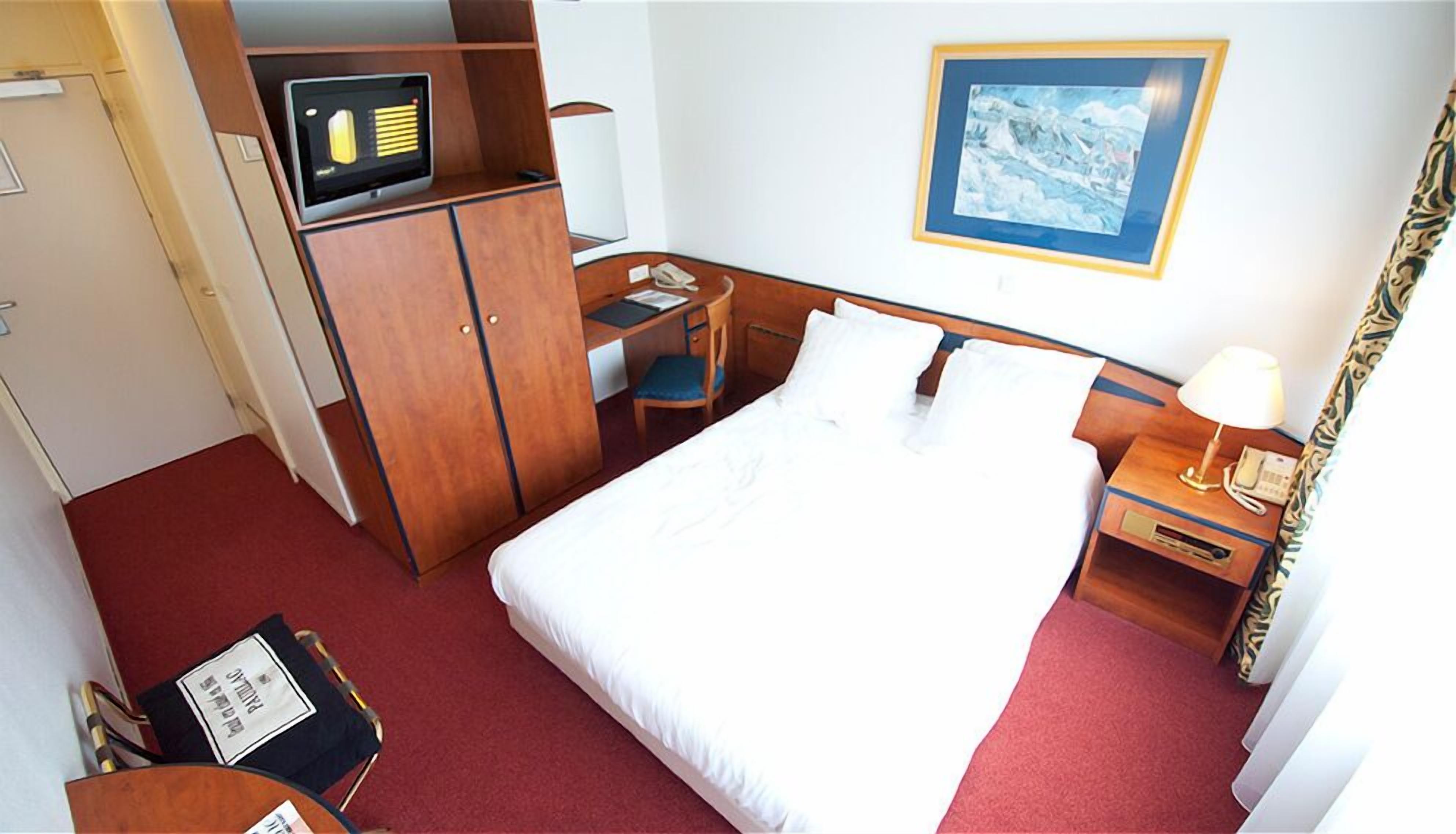 A hotel room with a bed, desk, and wardrobe.