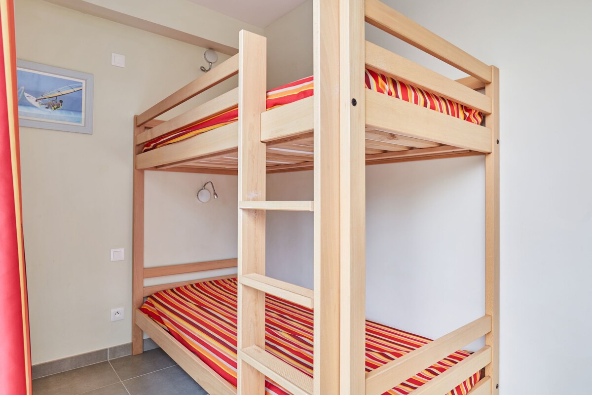 A bunk bed room with a striped mattress, a framed picture on the wall, and a light switch.