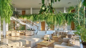 A spacious living area with a staircase, multiple seating arrangements, and abundant indoor plants. - Caloura Hotel Resort (Lagoa)
