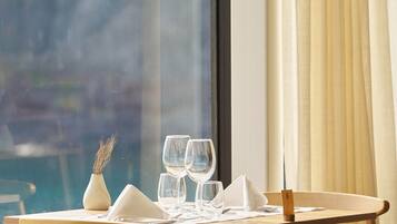 Una mesa de comedor con servilletas blancas, dos copas de vino y un florero con plantas secas.