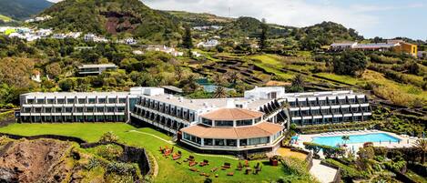 Un hotel moderno con un edificio central circular, rodeado de exuberantes jardines y una piscina.