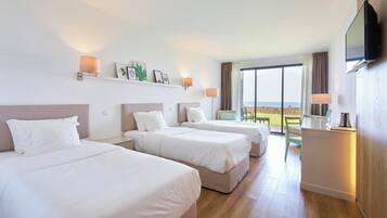Ein Hotelzimmer mit drei Betten, einem Fernseher, einem Schreibtisch und einem großen Fenster mit Blick.