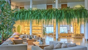 A spacious lobby with multiple seating areas, a marble reception desk, and hanging greenery. - Caloura Hotel Resort (Lagoa)