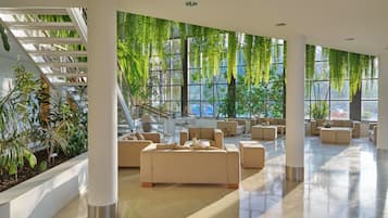 Un'ampia hall dall'arredamento moderno, con un'area salotto centrale con divani e una scala con ringhiera in vetro.