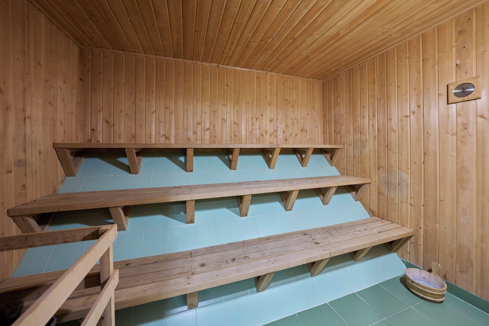 A wooden sauna with three benches and a small basin.