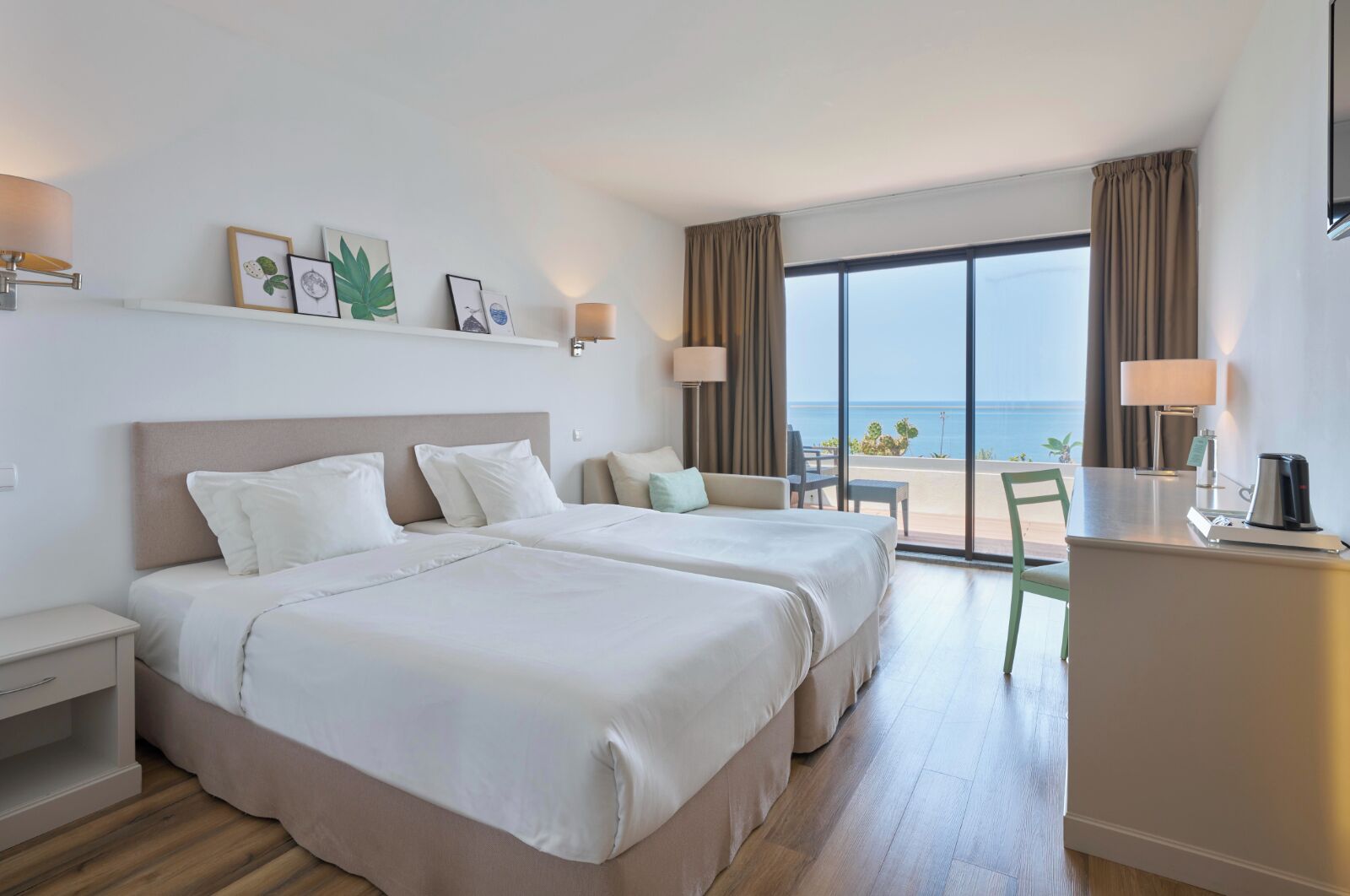 Een hotelkamer met twee bedden, een bureau, een stoel en uitzicht op zee.