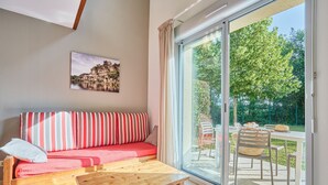 A modern living room with a sofa, a wooden table, and a large sliding glass door leading to an outdoor area with a table and chairs.