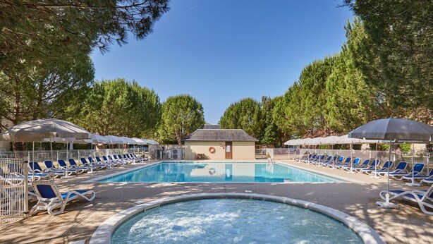 A swimming pool with lounge chairs and umbrellas, surrounded by trees.