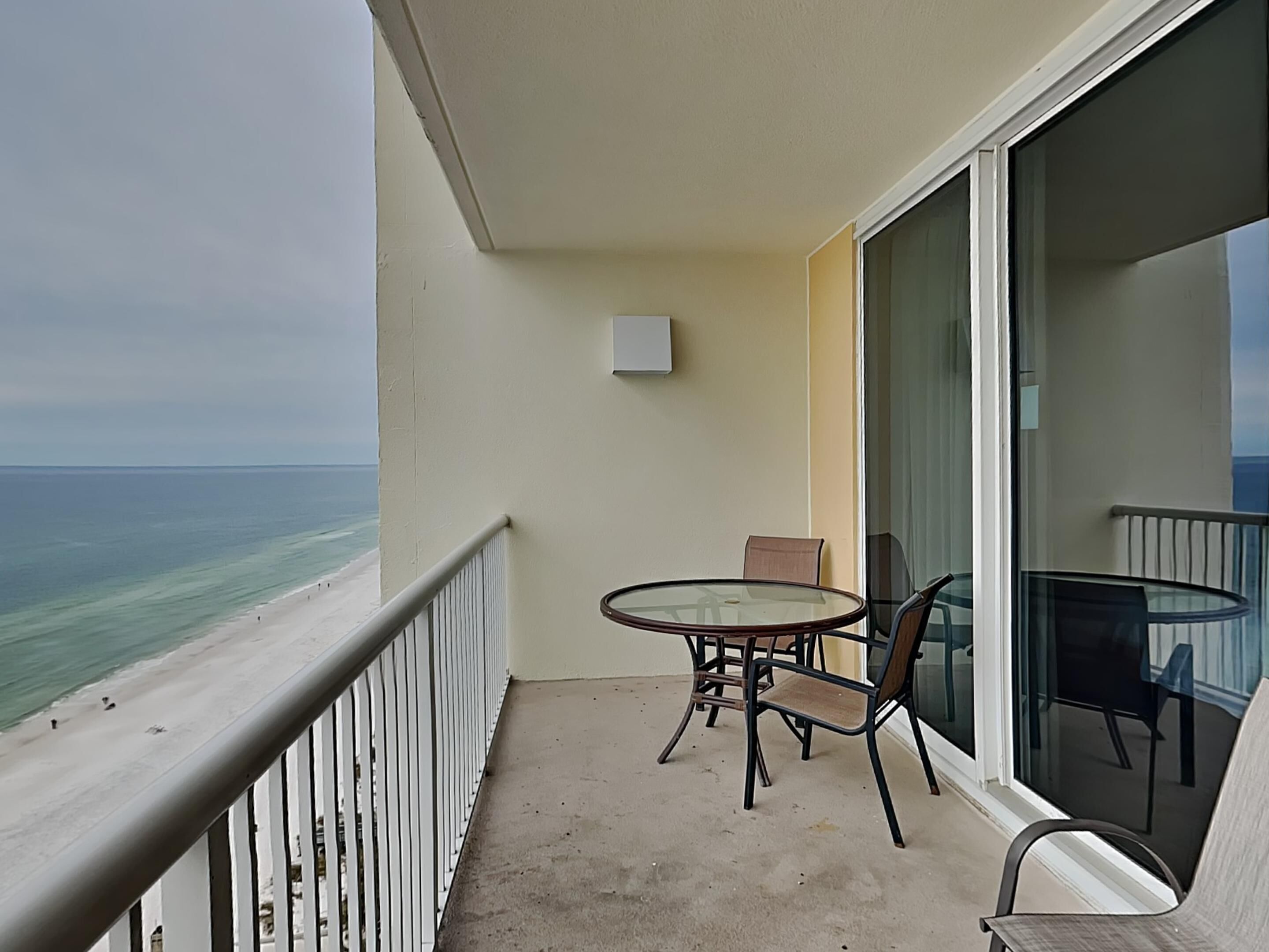 A balcony with a glass table and chairs, overlooking a beach and ocean.