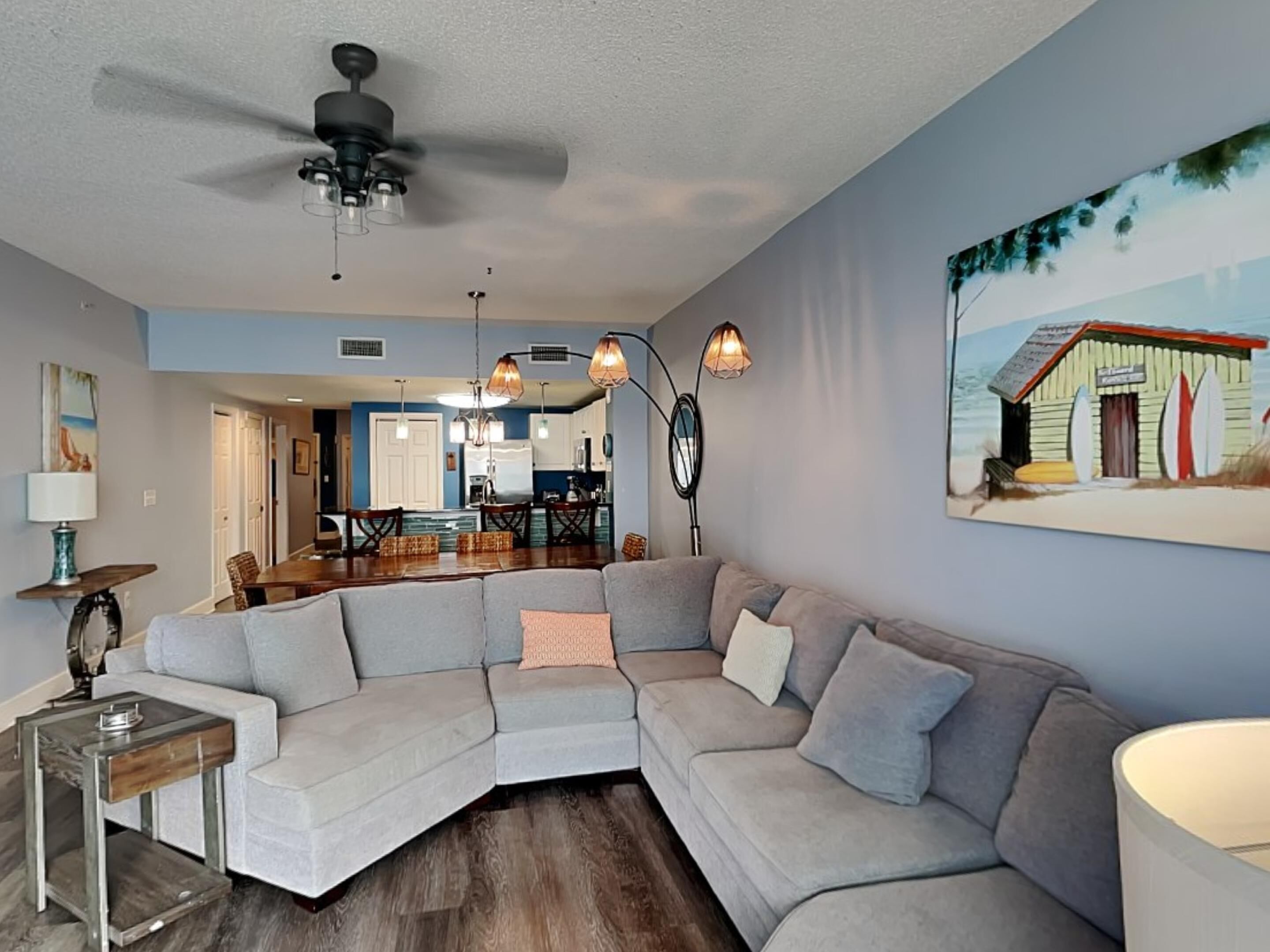 A living room with a sectional sofa, a dining table, and a kitchen in the background.